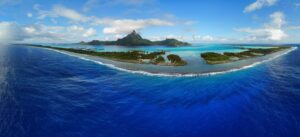 Aerial panoramic landscape view of the island of Bora Bora in French Polynesia with the Mont Otemanu mountain surrounded by a turquoise lagoon, motu atolls, reef barrier, and the S