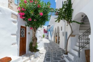 Enge Gasse mit weißen Häusern und Blumen auf einer Kykladeninsel