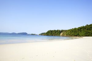Menschenleerer Strand vor bewaldeten Hügeln