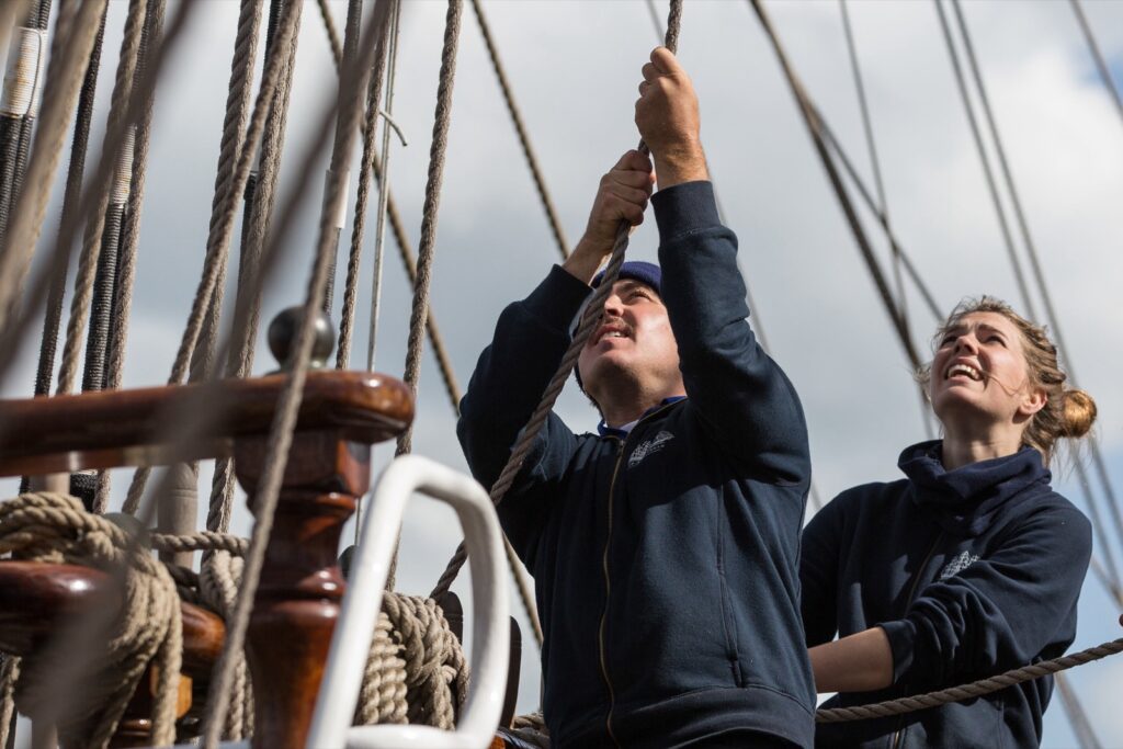 Crew holt gemeinsam eine Leine an Deck eines Großseglers