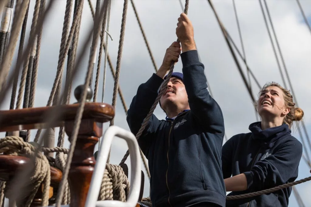 Crew holt gemeinsam eine Leine an Deck eines Großseglers